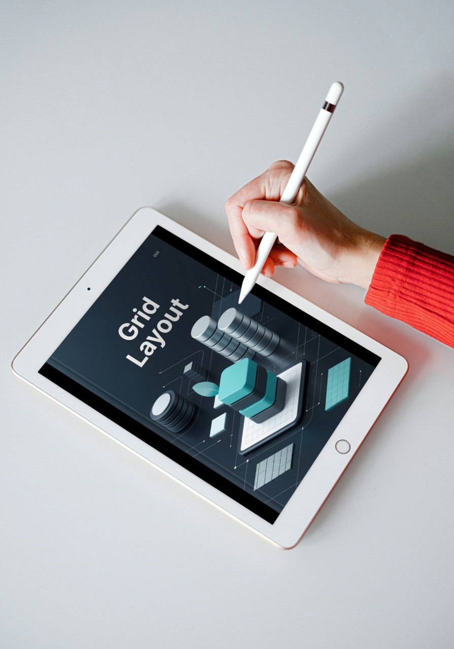 Hand holding a stylus over a tablet displaying a grid layout on a gray background